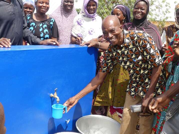 Ali Salifou, Direktor der Primarschule, nimmt freudig Wasser aus der realisierten Wasserstelle auf seinem Schulgelände 